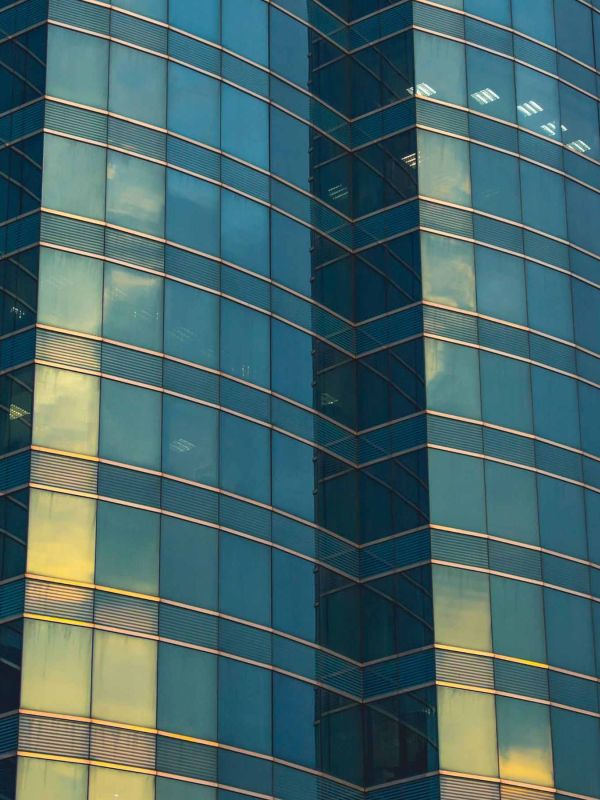 Vue en contre-plongée d’un immeuble en verre reflétant le ciel, illustrant la gestion et l’entretien des centres administratifs et commerciaux.